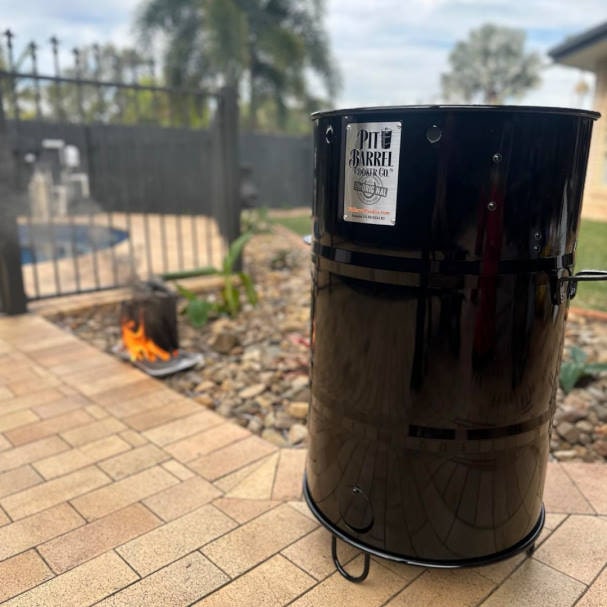 pit barrel in backyard with a chimney full of charcoal burning in