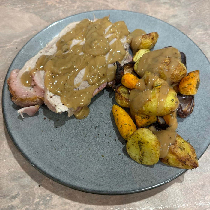 Rotisserie Roast Pork served on a plate with roast veggies and gravy