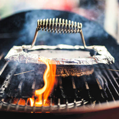 Cast Iron Burger Press | front view of burger press wrapped in alfoil pressing down a patty on a bbq