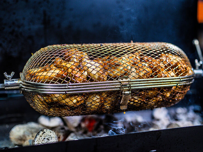 Rotisserie Tumbler Basket | close up view with wings and chips over coals