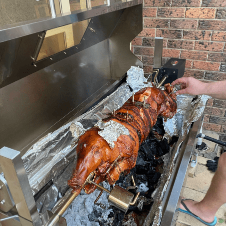 a whole pig on a spit roaster rotisserie fully cooked with someone checking the temperature using a thermometer