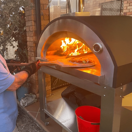 A premium pizza oven showing the flame burning and someone putting a fresh pizza inside